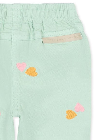 Pantalon à taille élastique vert clair avec des cœurs brodés roses et orange et une petite étiquette beige Stella McCartney.
