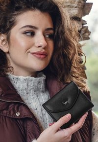 Schwarze Ledergeldbörse mit einem Klappenverschluss, ausgerüstet mit silbernen Beschlägen und einem Logo. Das Design ist kompakt und hat eine glatte Oberfläche.