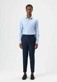 Lichtblauw overhemd met lange mouwen en kraag, gecombineerd met donkerblauwe, op maat gemaakte broek. Zwarte schoenen maken de outfit compleet. Eenvoudig, nauwsluitend ontwerp.