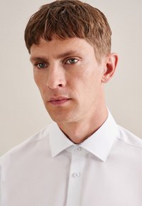 Witte shirt met puntkraag, blauwe accentstiksels en knoopsluiting. Glad stof met een klassieke pasvorm en zonder patronen.