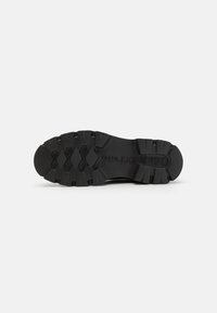 Semelle de chaussure en caoutchouc noir avec un motif de semelle robuste, comportant des crampons multidirectionnels pour une traction optimale et une surface texturée pour une bonne adhérence.
