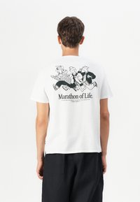 White cotton t-shirt featuring a black cartoon graphic on the back with three figures running and text "Marathon of Life." at the bottom.