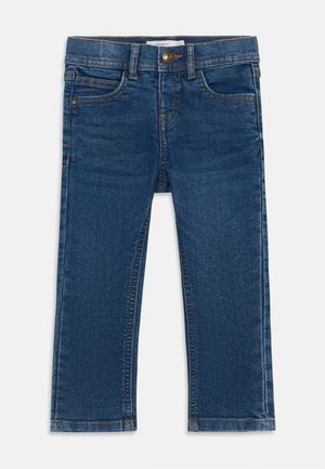 Mørkeblå denimjeans med rett snitt, med frontknapping, beltehemper og fem lommer. Avslutningen inkluderer gul søm.
