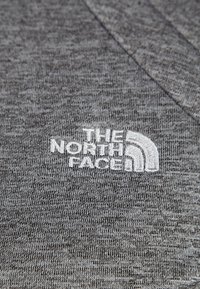 Šedé textilní tričko s texturovaným vzhledem a na spodním levém rohu bíle vyšitým logem "THE NORTH FACE".