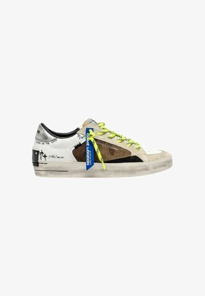 Zapatilla baja con paneles beige, blancos y marrones, cordones amarillos neón, talón negro, gráficos de palmeras y una etiqueta azul en los cordones.