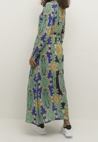 Lungo abito maxi con stampa floreale multicolore, dotato di vita aderente, maniche lunghe e una silhouette fluida. Abbinato a sneakers bianche e nere.