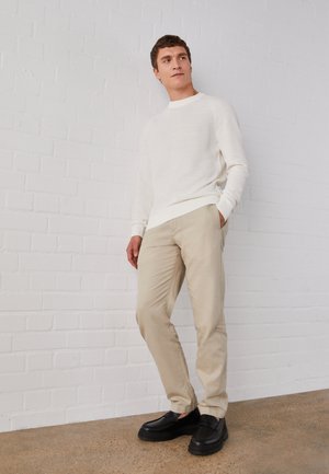 Cream knit sweater, beige chinos, and black shoes. The sweater features a ribbed hem and cuffs, while the chinos have a smooth texture.