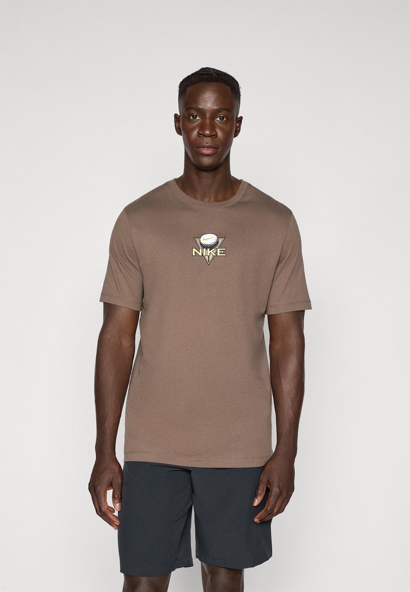 T-shirt en coton marron à manches courtes, avec un col rond et un logo graphique central en jaune et blanc. Associé à un short sombre.