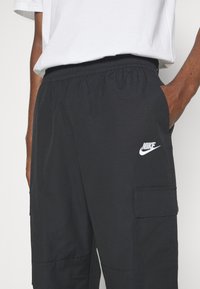 Black cargo pants made of lightweight fabric, featuring an elastic waistband, side pockets, and a small white Nike logo.
