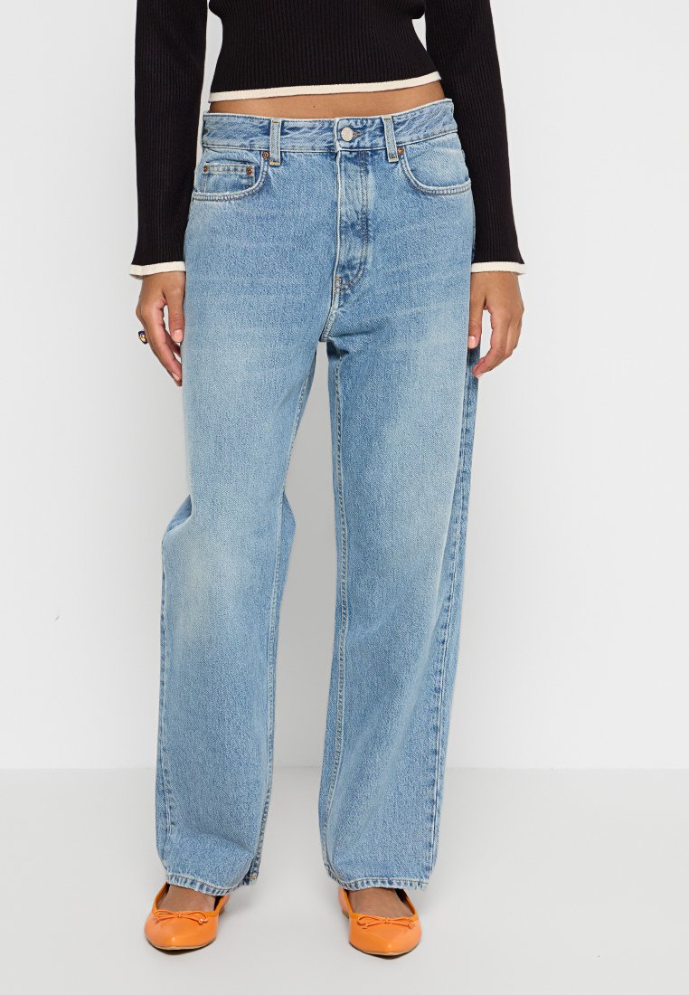 Helle blaue weit geschnittene Jeans aus Denim mit klassischem Fünf-Taschen-Design, subtilen Verwaschungen und hoher Taille. Getragen mit orangefarbenen Ballerinas.