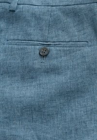 Blue textured fabric with a subtle check pattern, featuring a single black button at the waist and a back pocket with stitching details.