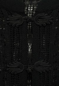 Schwarzes Strickkleid mit strukturiertem Muster und offenen Maschen. Auffällige Details sind dekorative schwarze Bindebänder am Halsauschnitt.
