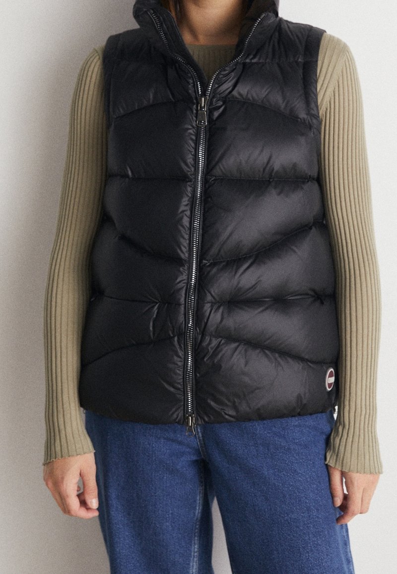 Gilet nero gonfio con zip frontale, caratterizzato da un colletto alto, design trapuntato e un piccolo etichetta logo sul lato destro inferiore.