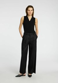 Black sleeveless top with a v-neck, paired with high-waisted black wide-leg trousers and black slip-on shoes. Smooth fabric with pleats.