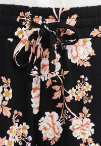 Zwarte bloemenbroek met een trekkoord in de taille. Voorzien van roze en witte bloemen met groene bladeren, gemaakt van een zachte, gestructureerde stof.