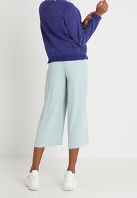 Fialový pletený svetr s dlouhými rukávy, v kombinaci s světlomodrými volnými kalhotami culotte a bílými teniskami. Svetr má texturovaný povrch.