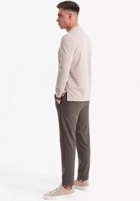Polo grigio chiaro a maniche lunghe con un motivo texturizzato, abbinato a pantaloni grigi scuri e sneakers grigio chiaro, visto da dietro.