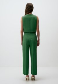 Haut sans manches vert associé à un pantalon vert taille haute. Le tissu semble lisse avec une coupe ajustée. La vue arrière montre des lignes épurées et un style minimaliste.