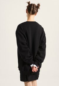 Black oversized sweatshirt with long sleeves, ribbed cuffs, and a crew neck. Worn over a black skirt, featuring a relaxed, soft texture.