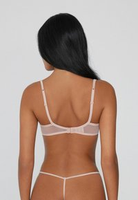 Jasnoróżowy, przejrzysty biustonosz z regulowanymi ramiączkami i zapięciem z tyłu. Gładka tekstura i minimalistyczny design bez widocznych wzorów.