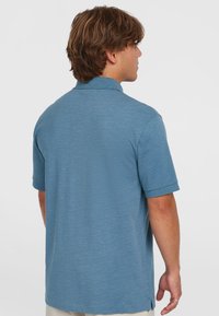 Polo tričko s krátkým rukávem, texturovaná světle modrá tkanina, design s límečkem, boční rozparky na lemu, minimální detaily na zadní straně.