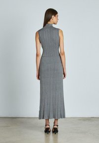 Ärmelloses graues Rippenstrickkleid mit hohem Kragen und plissiertem Rock, von hinten gezeigt. Es hat ein figurbetontes Oberteil und einen ausgestellt Saum.