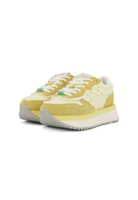 Zapatillas de ante amarillas con acentos de textil crema, cordones blancos y una gruesa suela de goma gris con un borde dentado.