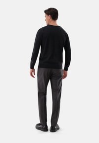 Dunkelgrauer Pullover mit Rundhalsausschnitt, kombiniert mit strukturierten grauen Hosen und schwarzen Schuhen. Das Outfit hat eine schmale Silhouette.