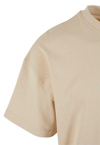 Beige T-shirt med en blød tekstur, korte ærmer og en klassisk rund hals. Har dobbeltstik for holdbarhed.