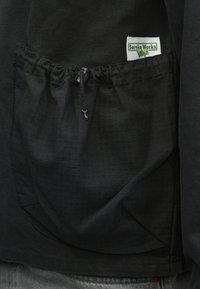 Čierna bunda s textúrovanou látkou, predným vreckom so sťahovacou šnúrkou a viditeľnou štítkom s nápisom "Service Works".