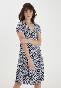 Sukienka w zwierzęcy wzór w kolorze granatowym i białym, z dekoltem w serek i krótkimi rękawami, posiadająca rozkloszowany, lejący się spódnicę oraz miękką, teksturowaną tkaninę.