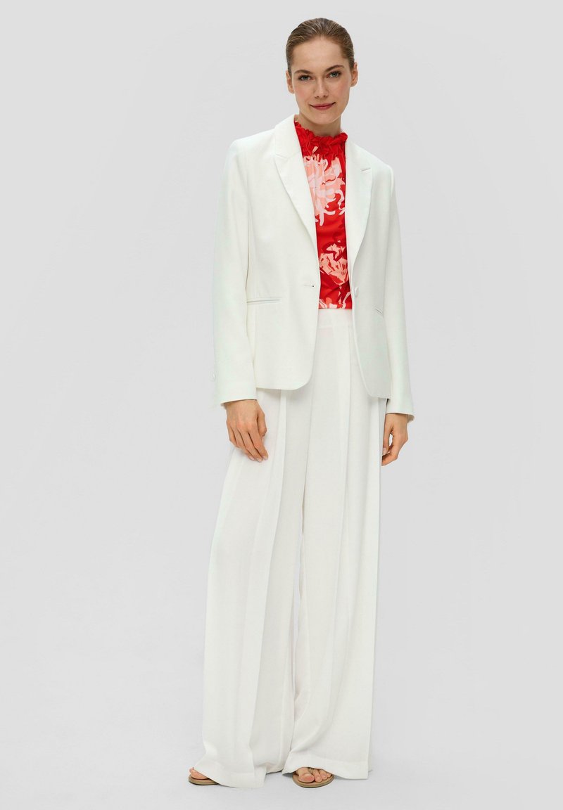 Witte op maat gemaakte blazer over een rode gebloemde top, gecombineerd met witte wijde broekspijpen. Soepele stof met een formeel ontwerp en verborgen sluitingen aan de voorkant.