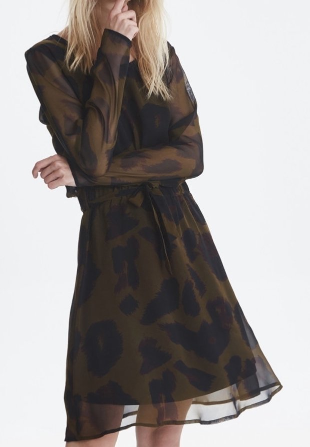 Femme portant une robe transparente à manches longues avec un motif abstrait sombre, cintrée à la taille avec une ceinture assortie.