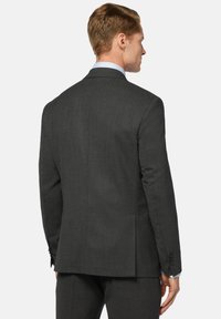 Veste de costume gris foncé en tissu texturé, avec une fente simple et des poignets boutonnés. Col de chemise bleu clair visible. Design épuré et ajusté.
