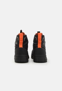 Des sneakers montantes noirs présentent une surface texturée, une tirette orange et des accents à motifs, avec une semelle en caoutchouc flexible.