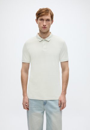 Jasnozielona koszulka polo z klasycznym kołnierzykiem, dwoma guzikami i krótkimi rękawami. Nosi się ją z jasnoniebieskimi, luźnymi dżinsami.