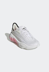 White athletic sneaker with a textured, knit upper, black accents, pink detailing on the sole, and a rounded toe design.