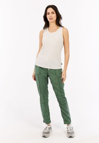 Canottiera beige chiaro con texture a coste, abbinata a pantaloni cargo verdi con dettagli di cucitura e scarpe da ginnastica grigie.