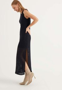 Abito in maglia blu navy con motivo a zig-zag, design senza maniche, spacco laterale e texture morbida, abbinato a stivali alla caviglia beige con tacco a stiletto.