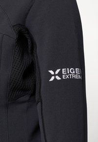 Černá bunda s texturovanou síťovinou uvnitř a logem "EIGER EXTREM" vyšitém bílou barvou na pravém rukávu. Obsahuje panelové švy.