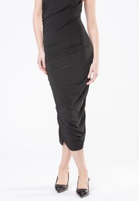 Vestido negro midi con una silueta ajustada, textura fruncida y tela suave. Combinado con tacones negros brillantes de punta afilada.