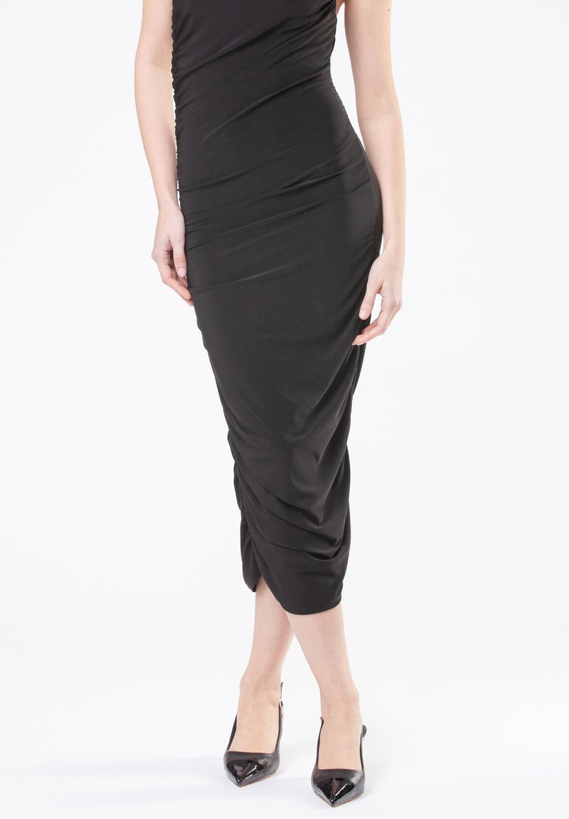Vestido negro midi con una silueta ajustada, textura fruncida y tela suave. Combinado con tacones negros brillantes de punta afilada.