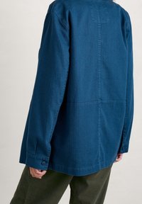 Dark blue, lightweight jacket with a relaxed fit, button cuffs, and visible seam details. Material texture appears smooth with a soft finish.