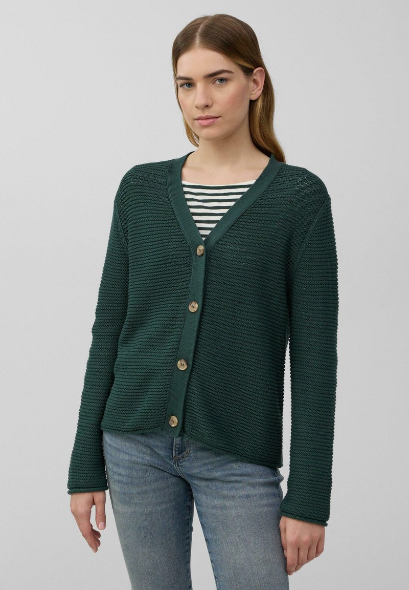 Grüne strukturierte Strickjacke mit V-Ausschnitt, knopflosem Verschluss und langen Ärmeln, getragen über einem gestreiften Hemd. Der Stoff hat ein geripptes Muster.