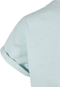 Chemise bleu clair à manches courtes avec détail de manches retroussées sur un fond blanc uni.