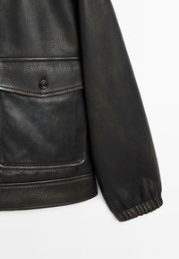 Giacca in pelle nera con finitura texturizzata; presenta una tasca frontale con bottone, polsini a coste e un colletto liscio.