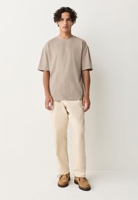 Lichtbruin textuurkorte mouw T-shirt gecombineerd met crèmekleurige broek en bruine suède schoenen met dikke zool.