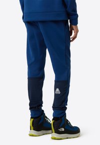 Temno modre športne hlače z teksturiranim panelom na spodnjem delu nog ter majhnim belim logotipom. Kombinirane z modrimi in črnimi pohodniškimi čevlji.