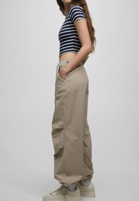 Pasiasty granatowo-biały crop top z krótkimi rękawami; beżowe, luźne spodnie z kieszeniami bocznymi i wiązaniem w talii; jasne sneakersy.