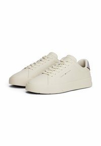 Sneakers in pelle beige con punta tonda, lacci piatti, suole testurizzate e dettaglio del logo sul lato. Design minimalista con una finitura liscia.